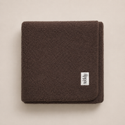 Folded brown fleece blanket with a brand label on a beige background