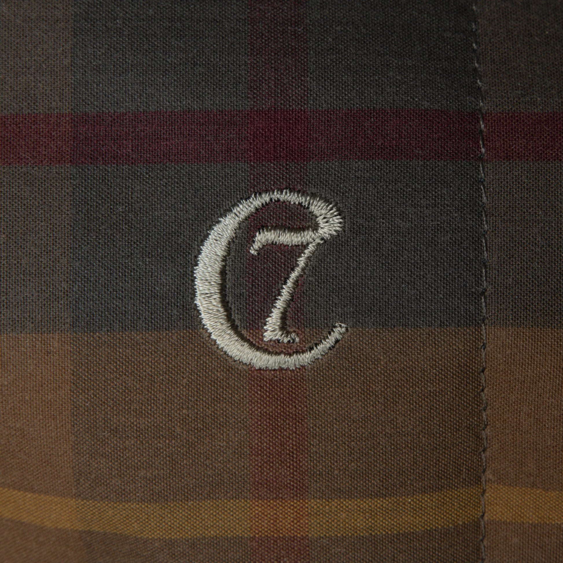 Close-up of a plaid fabric with a embroidered logo on a brown and black checkered background.