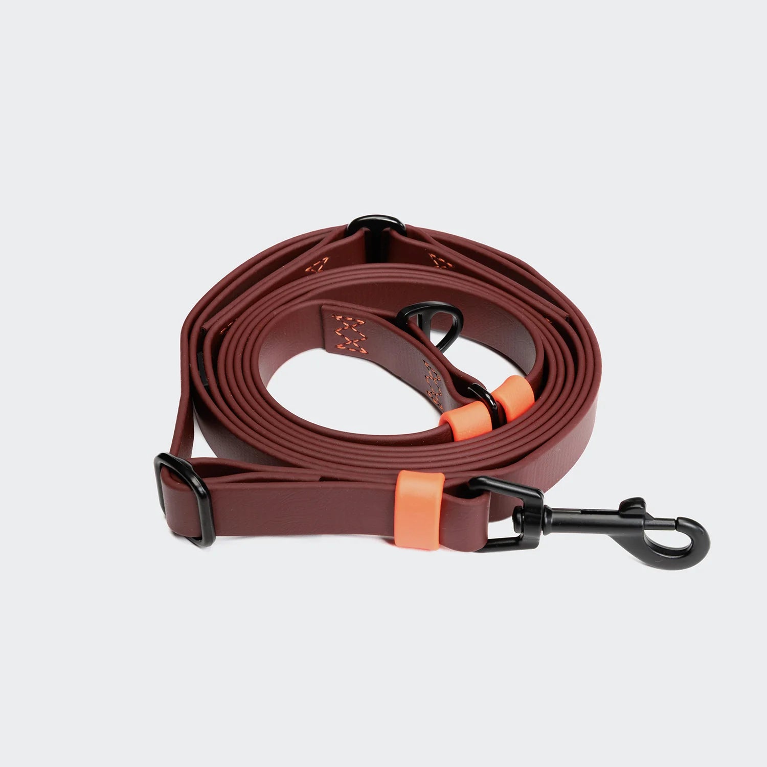 Brown dog leash with black clip and orange accents on a light gray background