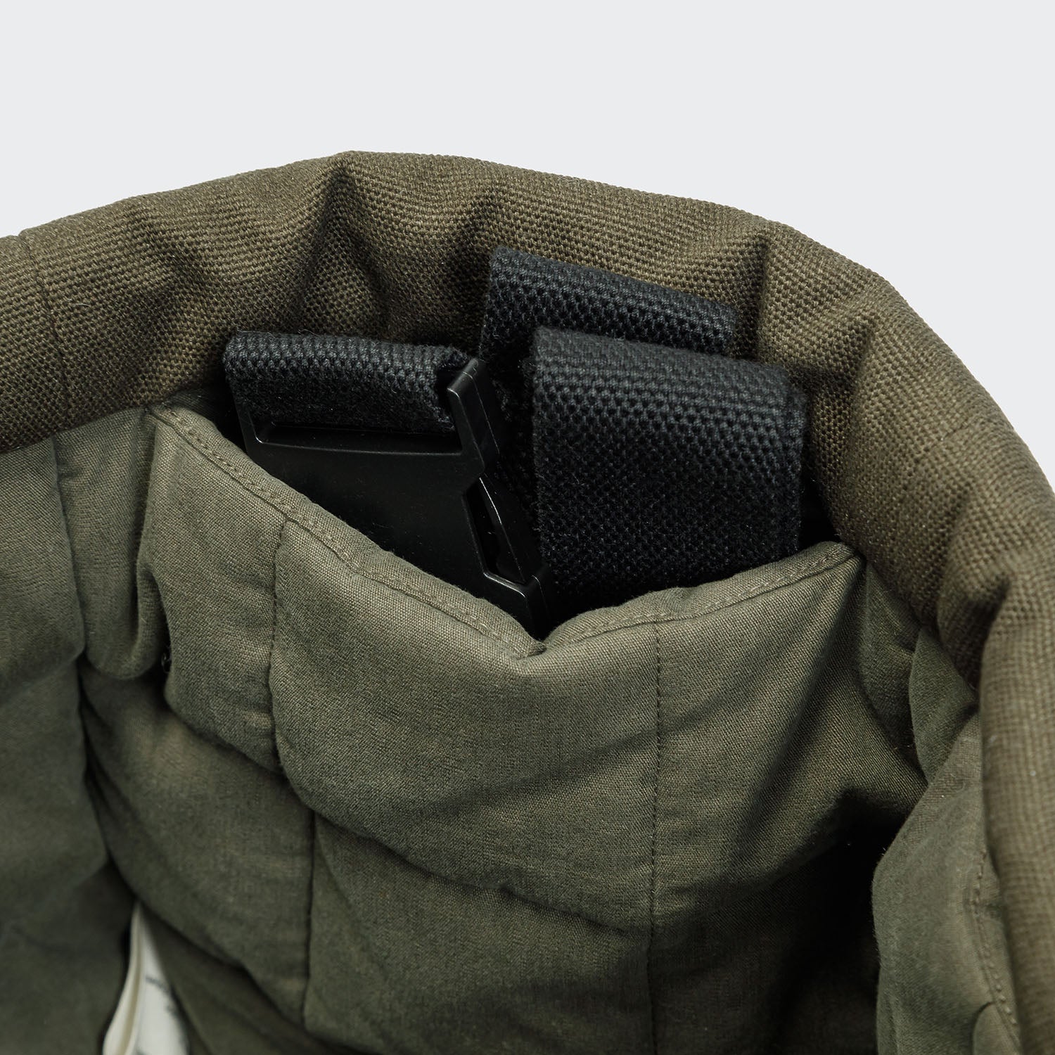 Close-up of green fabric with black straps inside, on a light gray background