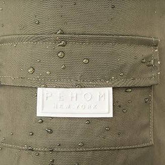 Close-up of an olive green waterproof fabric pocket with water droplets on the surface and a white rectangular 'PEHOM NEW YORK' brand label sewn onto the front.