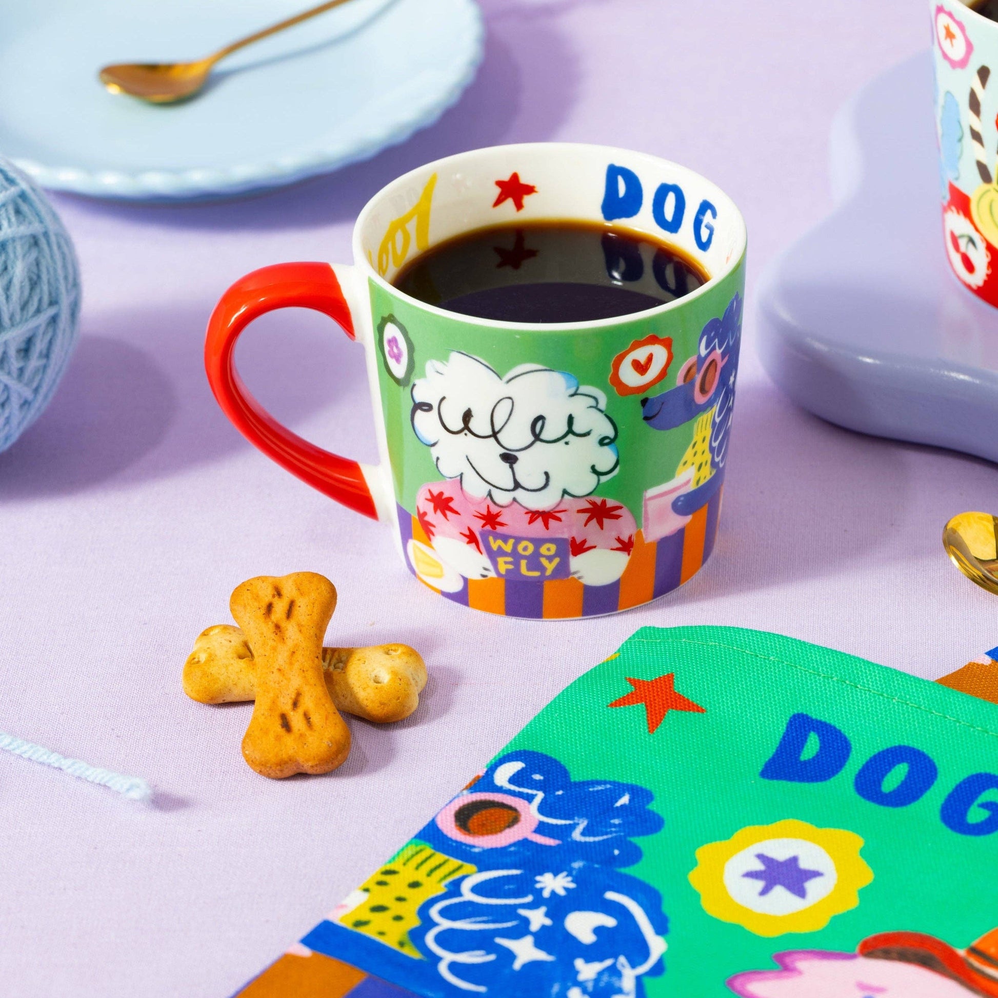 Colorful mug with dog-themed design on a table with cookies and a plate.