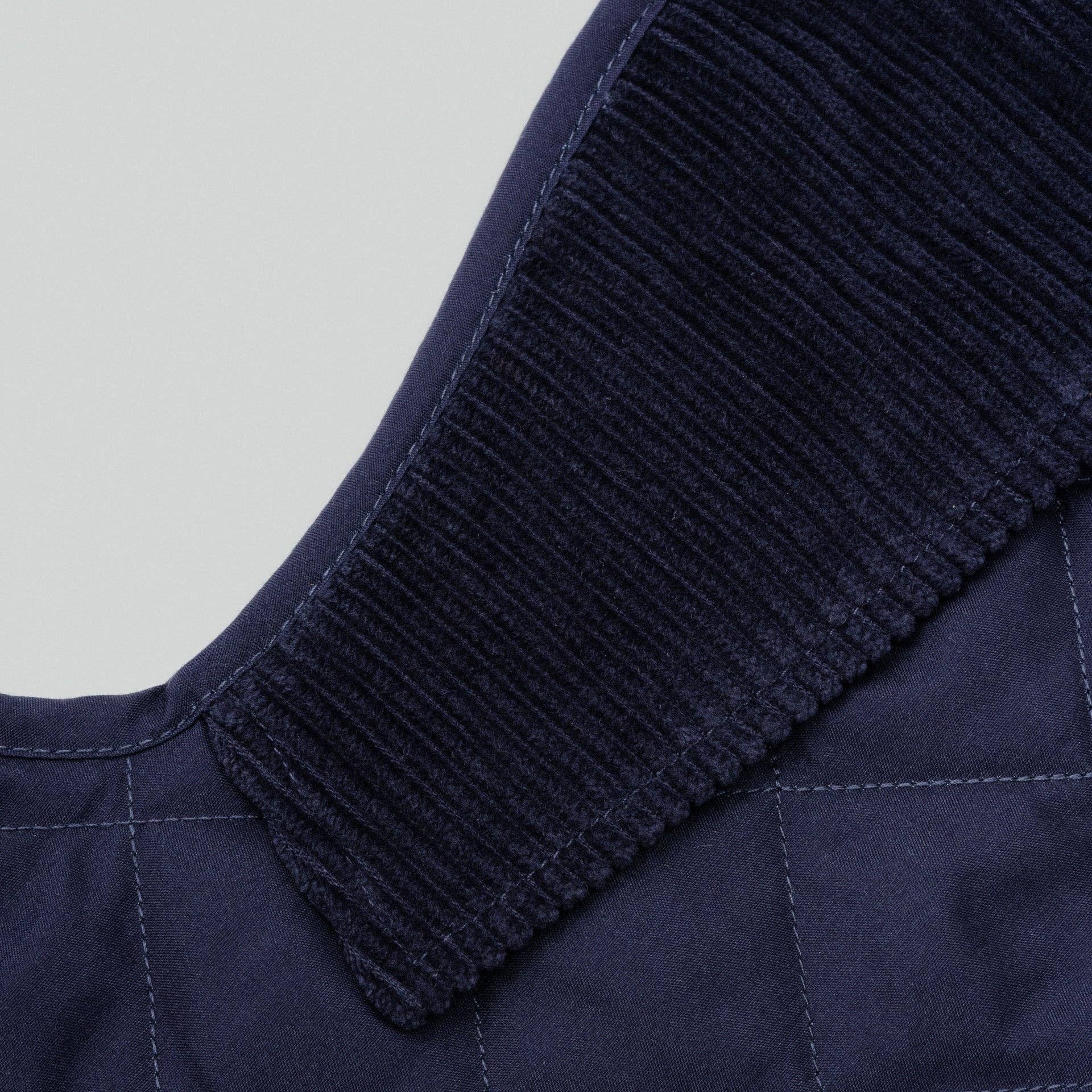 Navy quilted jacket with ribbed collar on a light gray background
