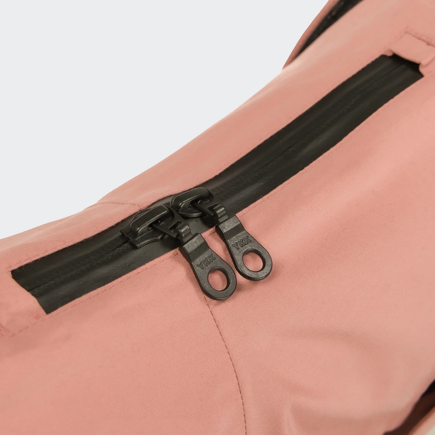 Close-up of a black zipper on a pink jacket against a light gray background