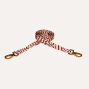 A zebra-print fabric dog leash with gold-tone metal swivel clasp hardware, shown coiled on a light cream background.