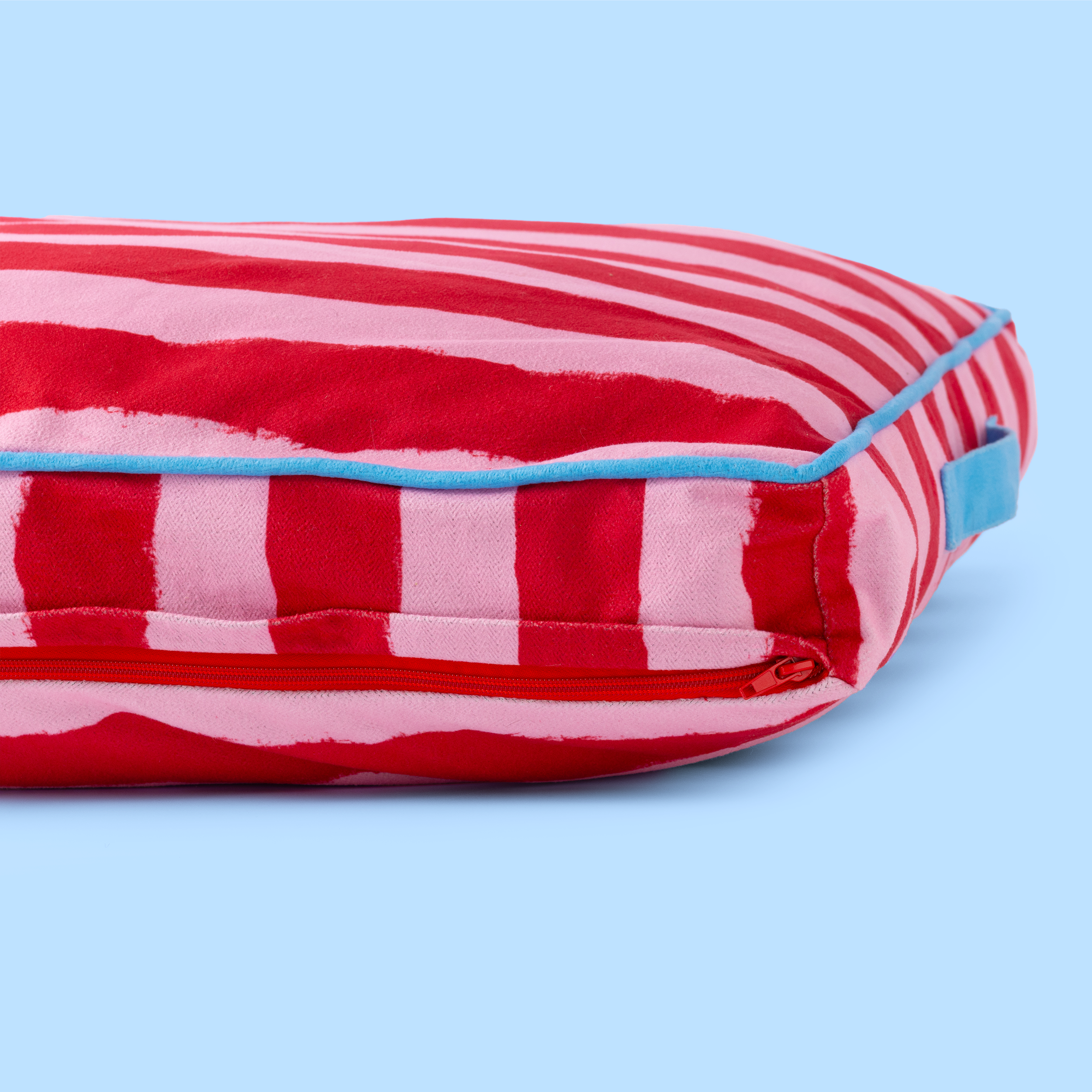 Red and pink striped pillow with blue edges on a light blue background
