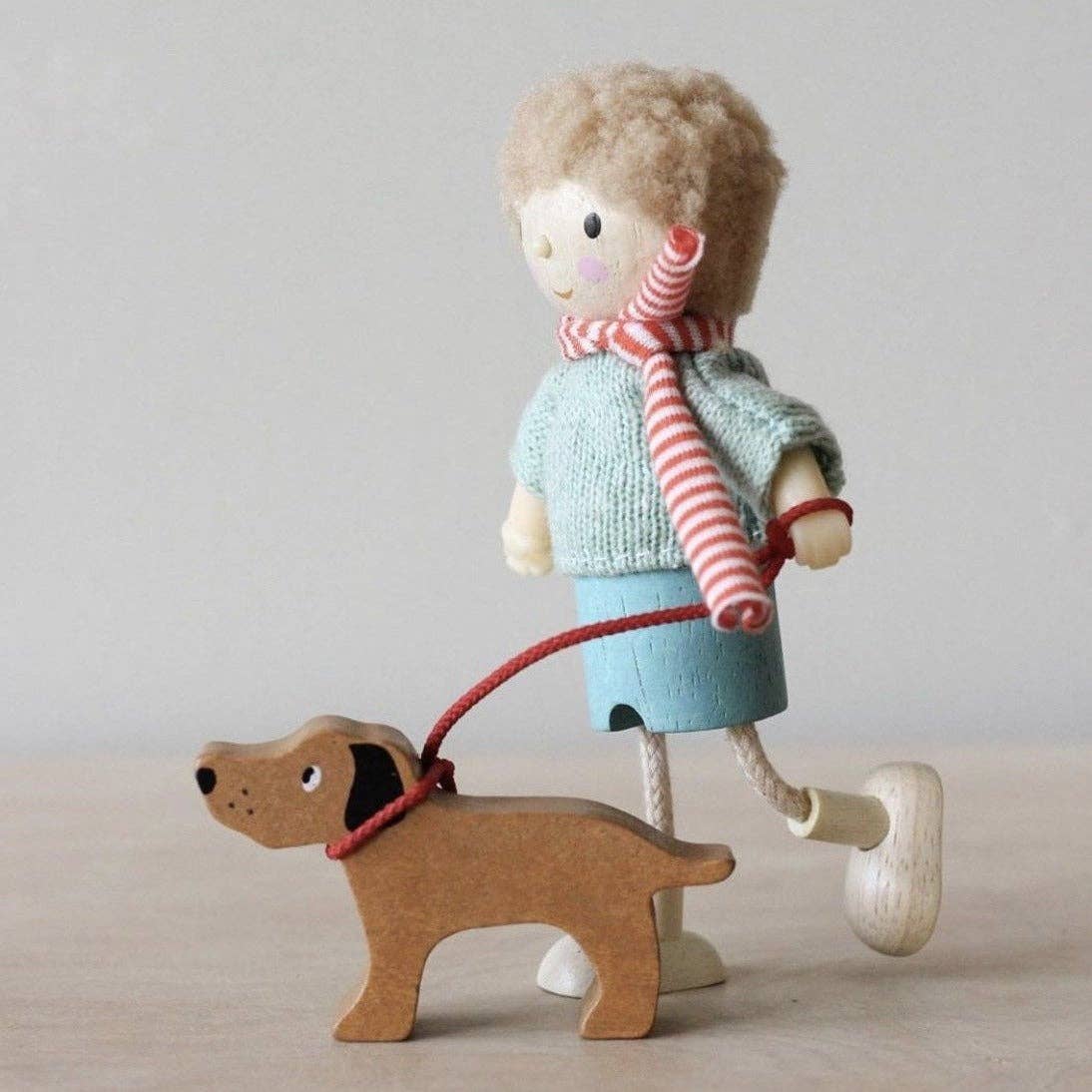 Wooden toy figure of a child with a dog on a leash against a plain background