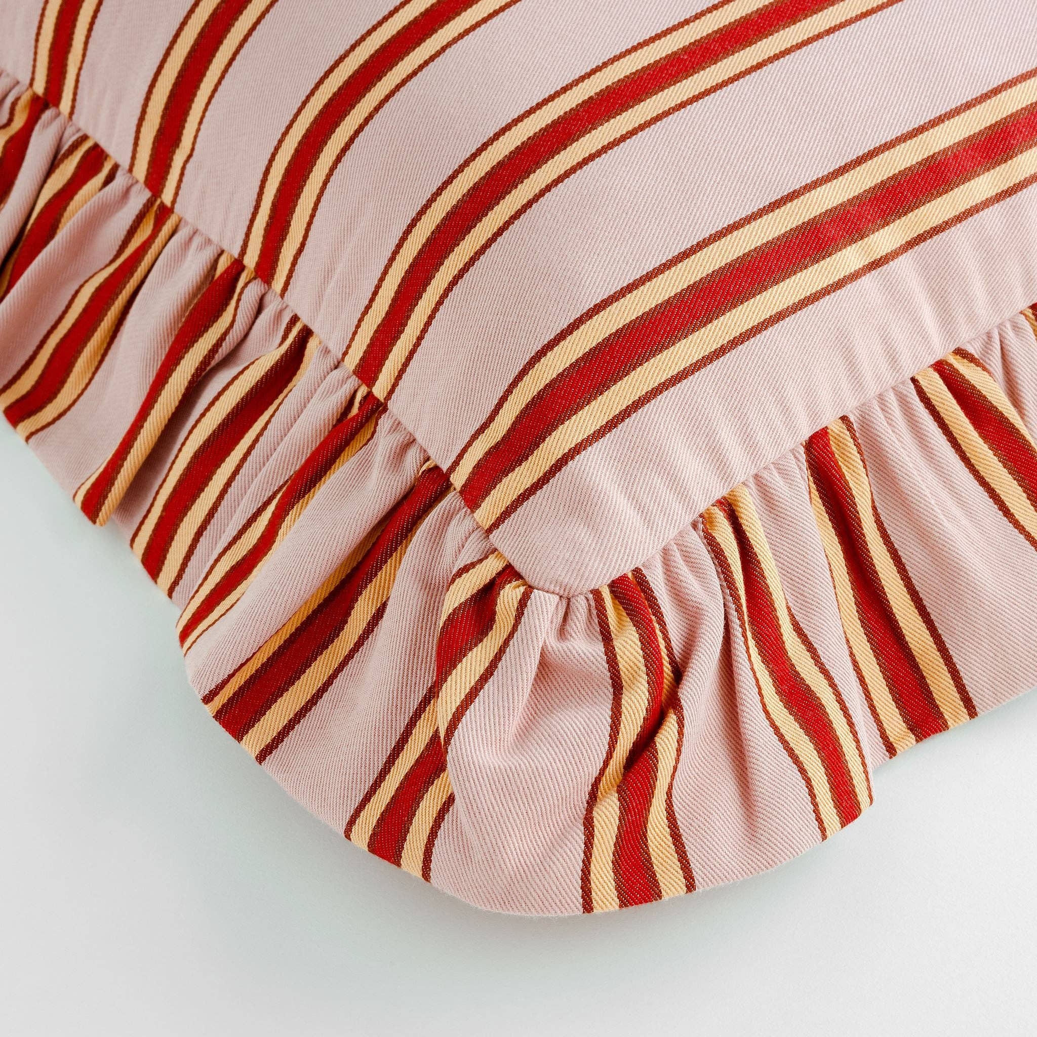 Pink striped designer cushion with red, peach and rust stripes and frilled trim.