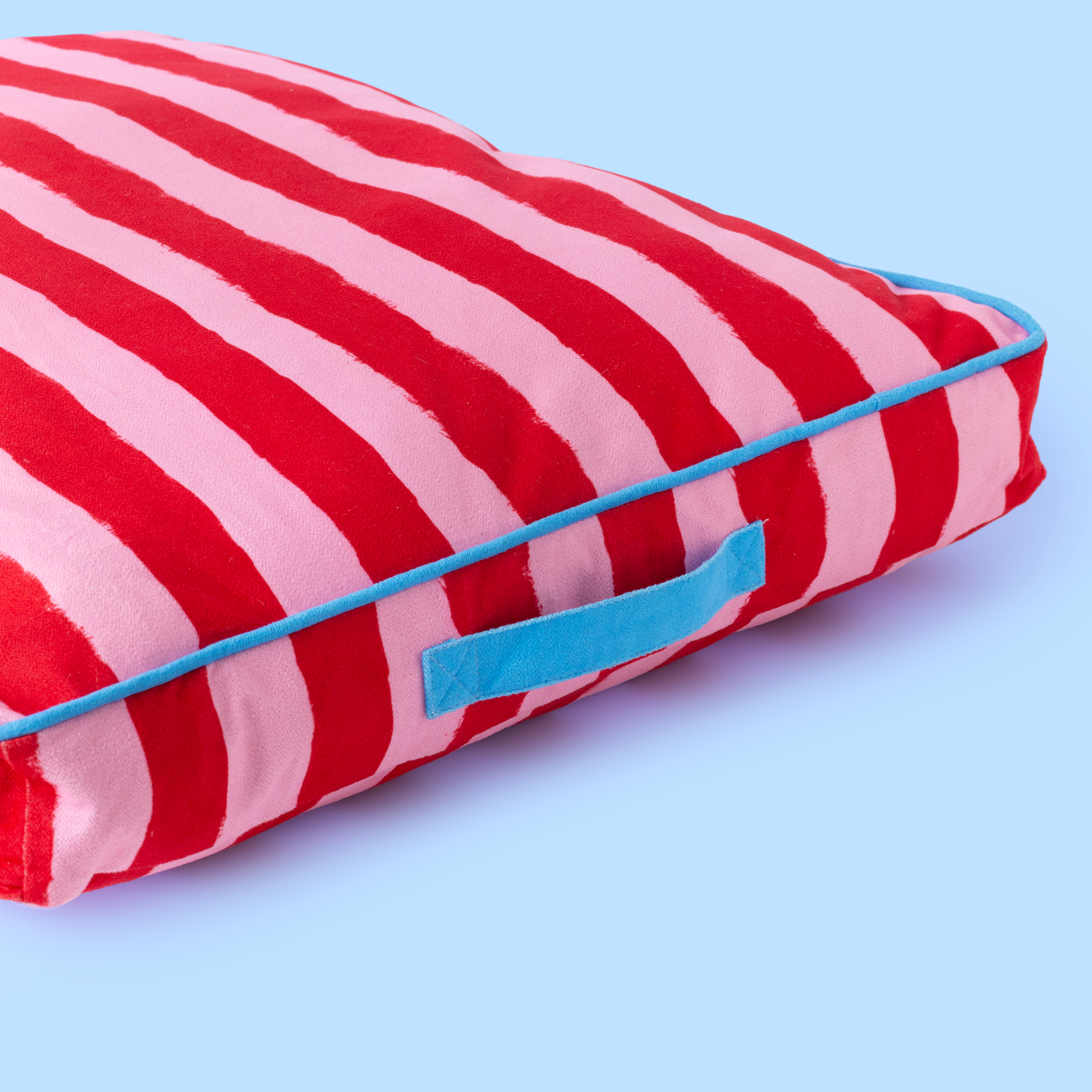 Red and pink striped pillow with a blue border on a light blue background