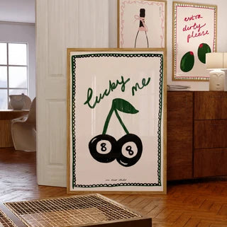 Framed artwork with 'lucky me' and cherries design in a room with wooden floor and furniture.