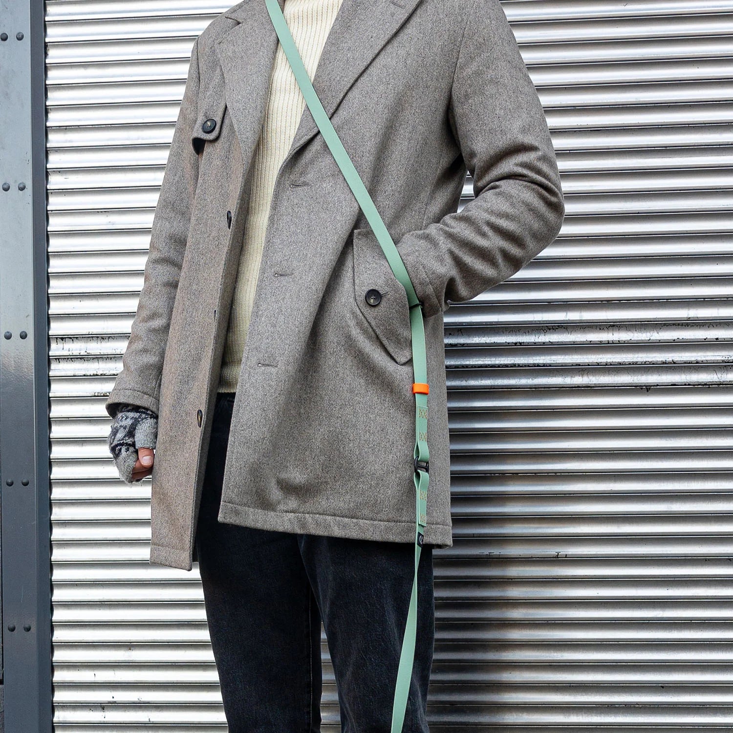 Person wearing a gray coat with a green strap over a metallic background