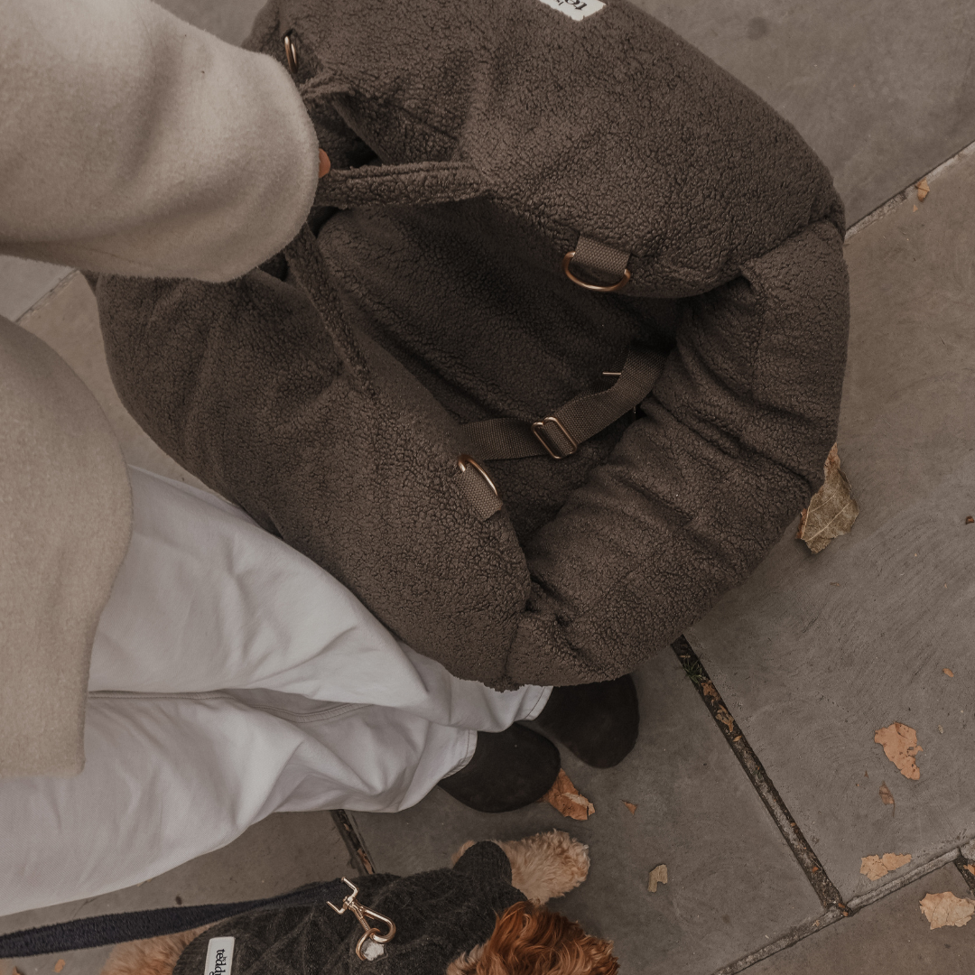 Brown textured backpack on a stone pavement with a person and dog in the background.