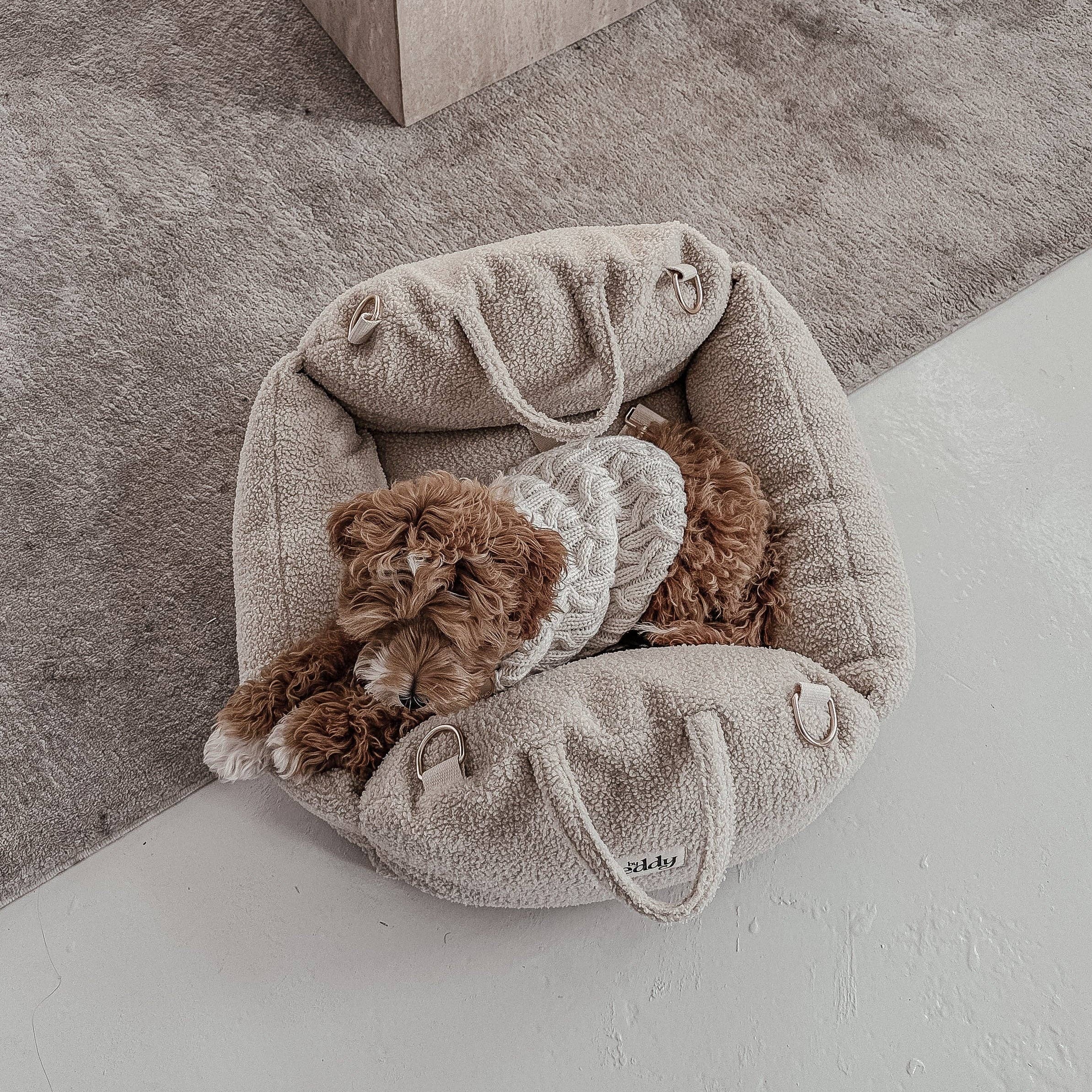 Small brown dog in a cozy beige pet bed on a light gray floor.