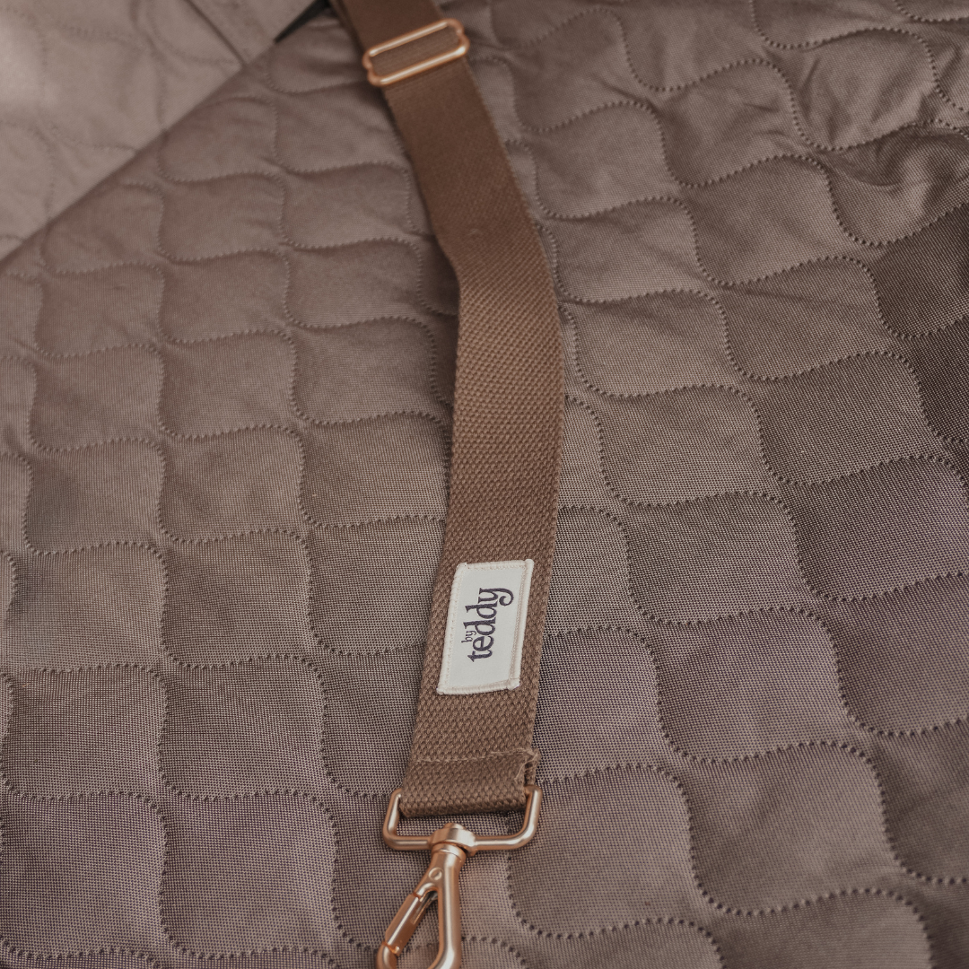 Brown quilted bag with a strap and visible brand label on a matching brown textured background
