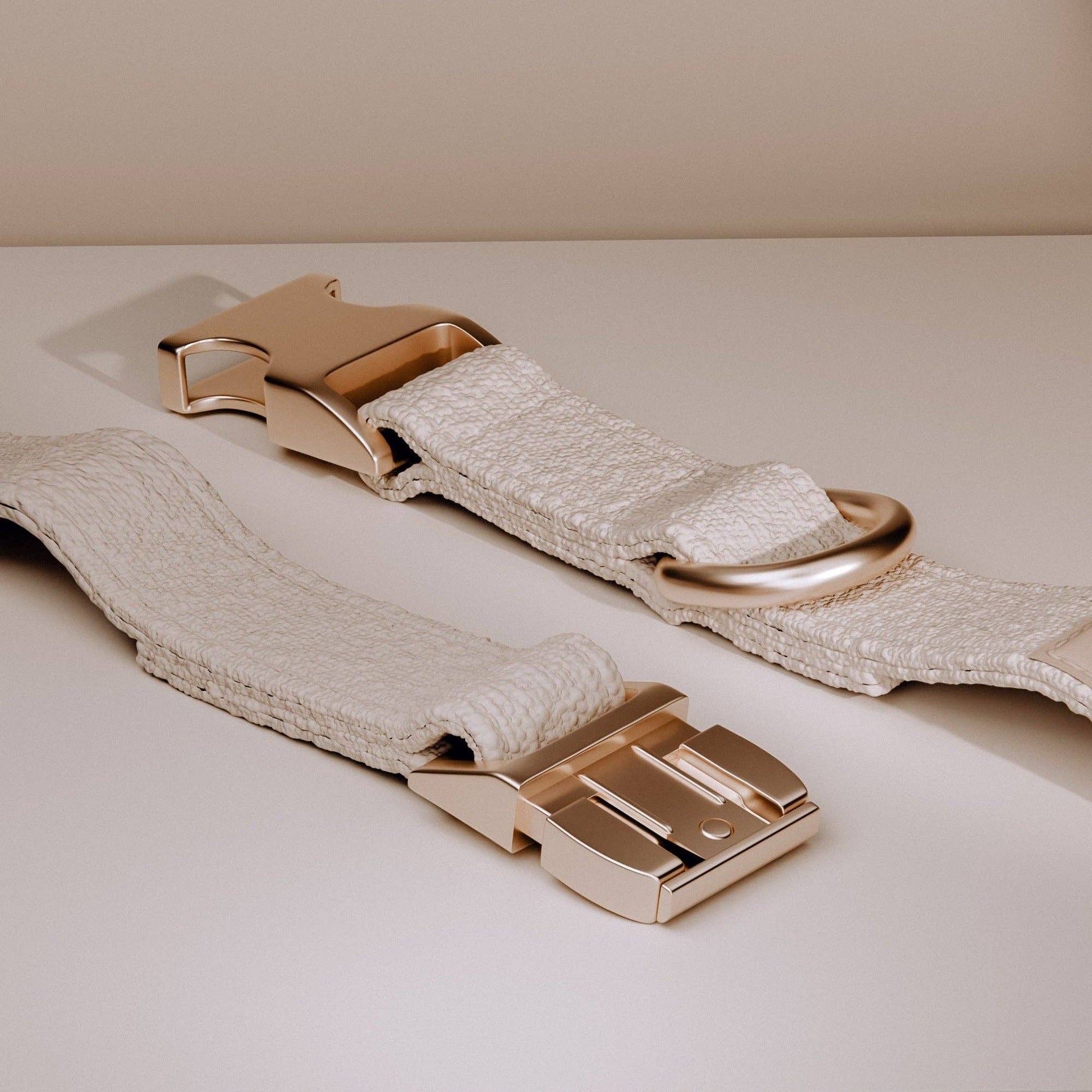Beige fabric belt with gold hardware on a light beige background
