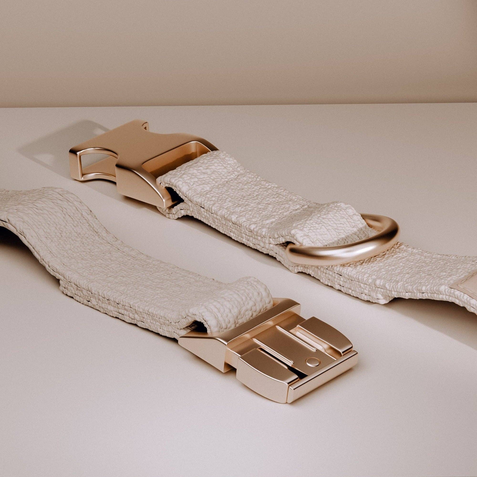 Beige fabric belt with gold hardware on a light beige background