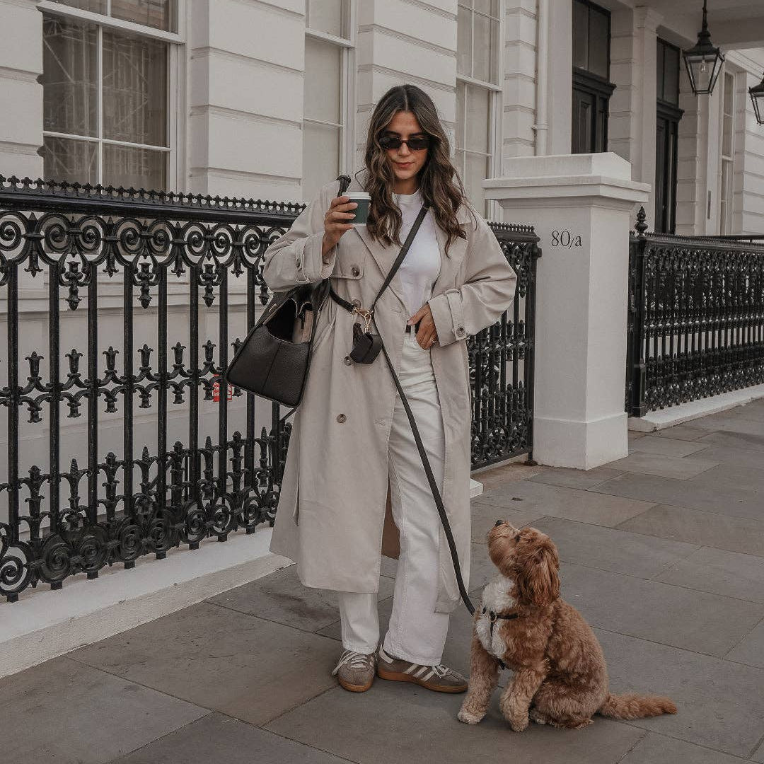 Woman in a trench coat with a dog on a leash in front of an elegant building.