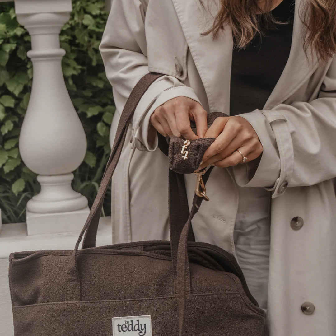 Person holding a brown tote bag with 'teddy' brand label, wearing a beige coat.