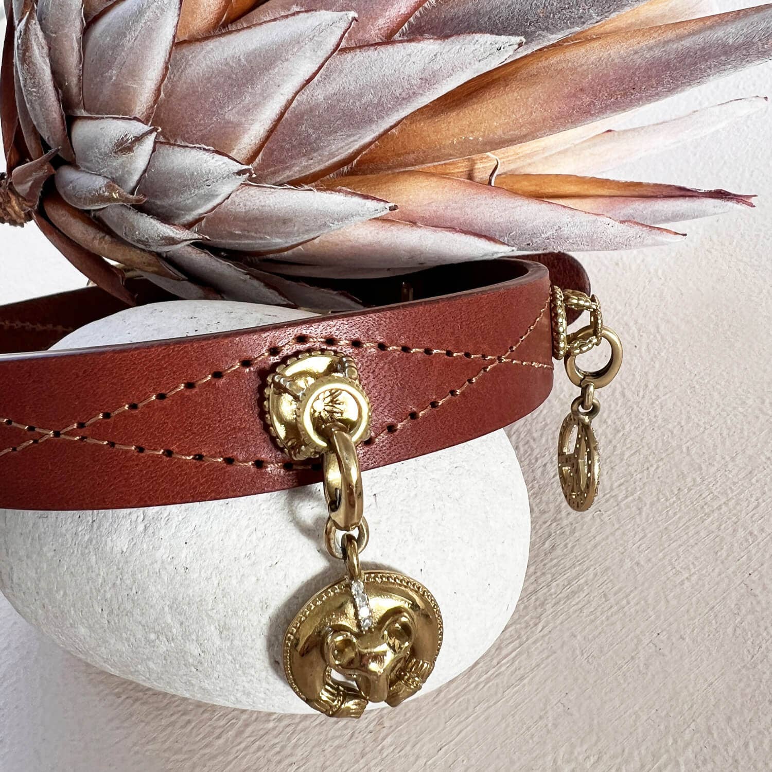 Brown leather bracelet with gold charm on a white surface