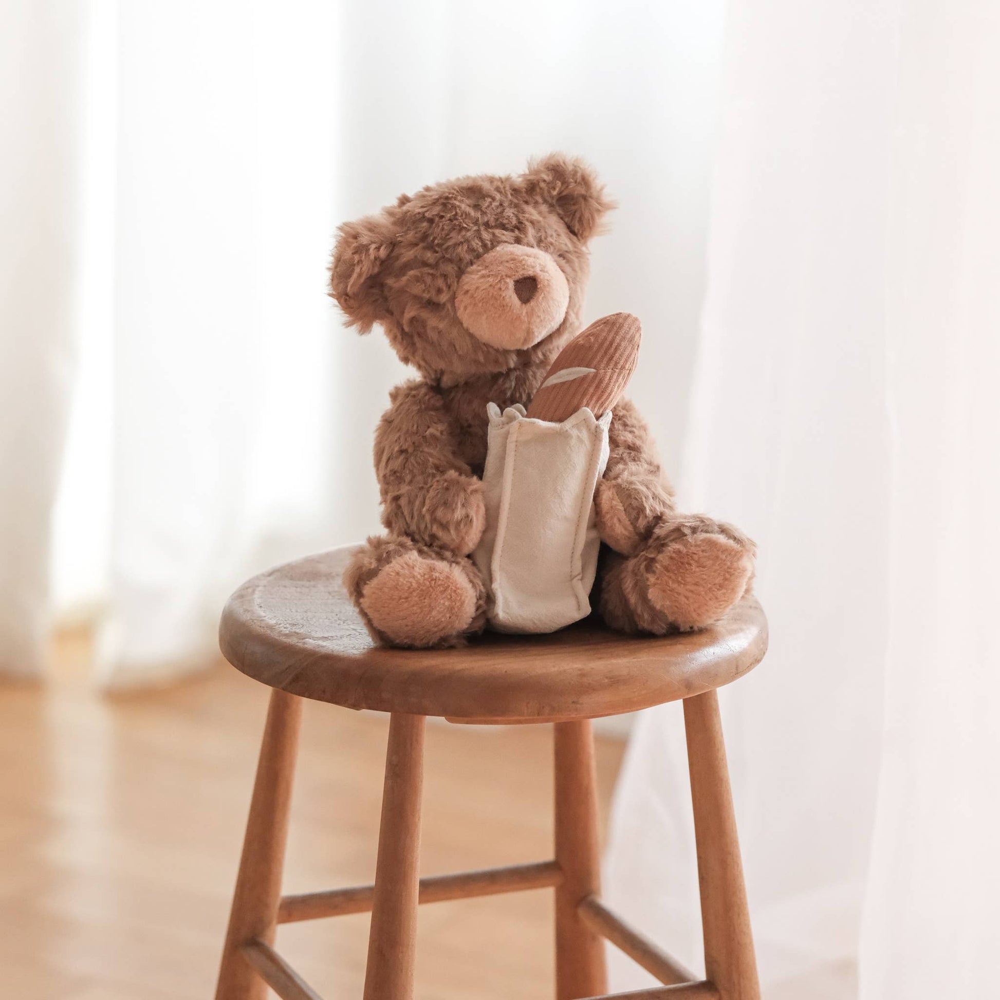 Brown teddy bear with a white bag on a wooden stool against a light background