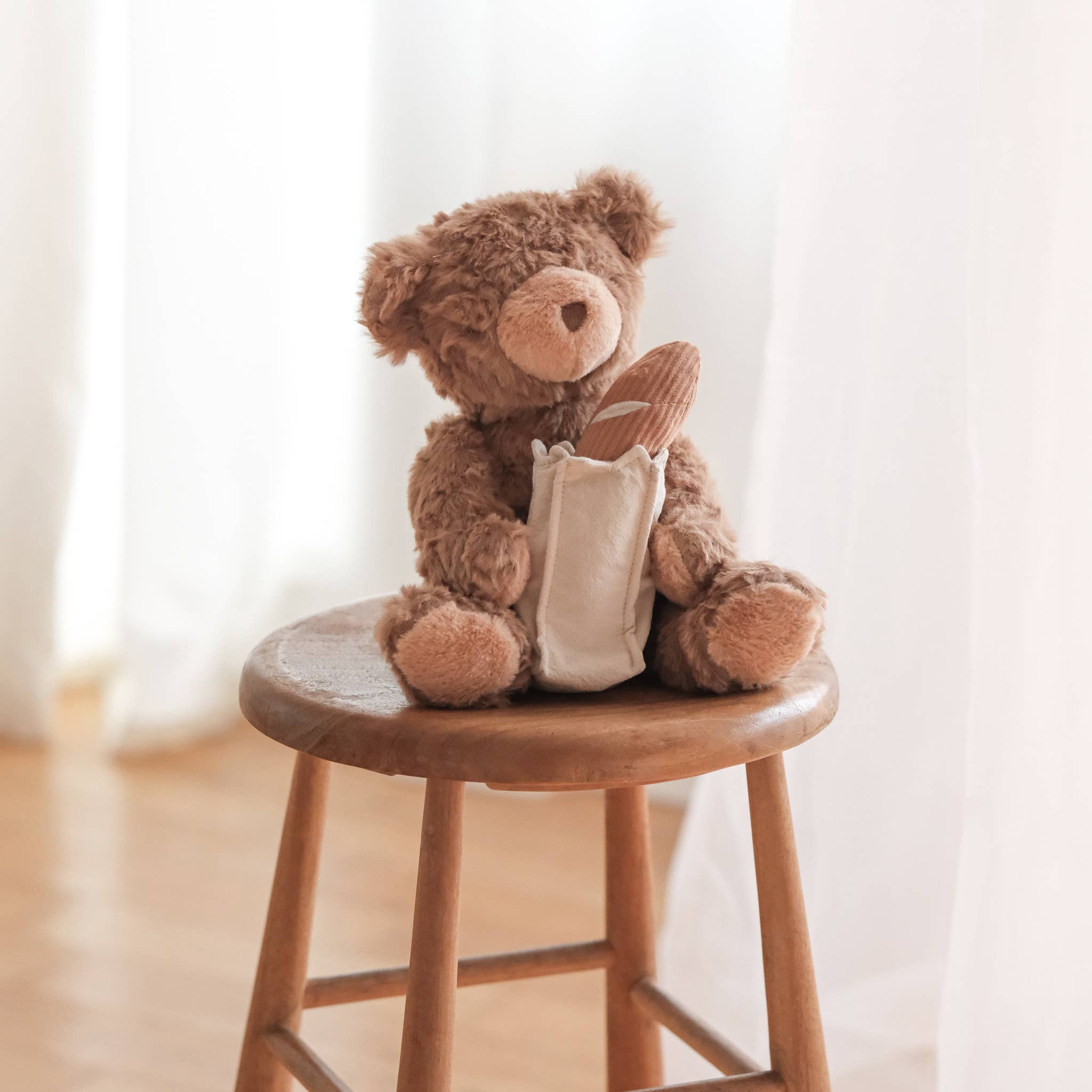 Brown teddy bear with a white bag on a wooden stool against a light background