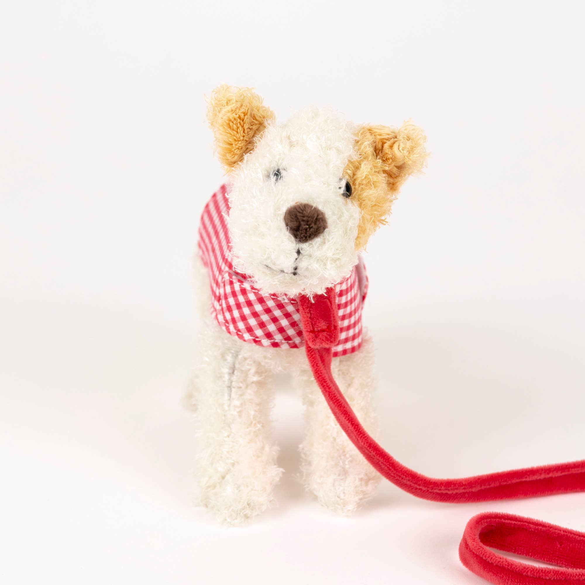Stuffed dog toy with a red checkered harness and leash on a white background