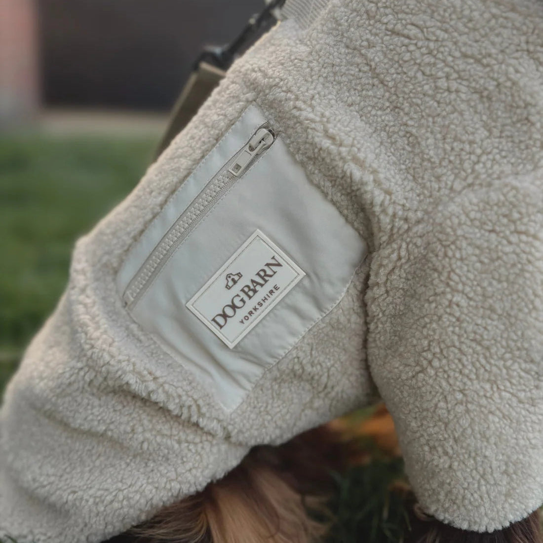 Close-up of a dog wearing a fleece coat with a visible brand logo on a grassy background