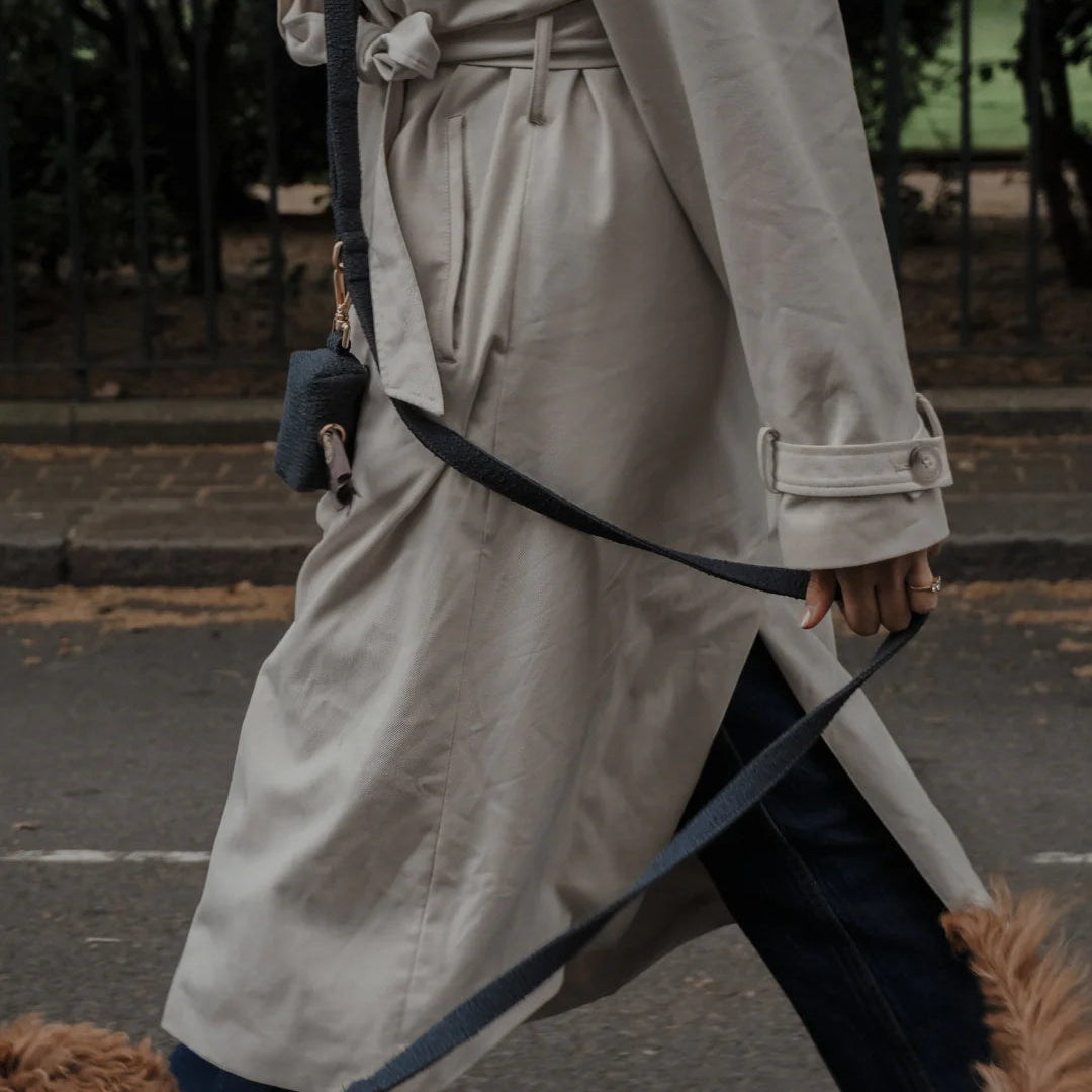 Person in a trench coat walking a dog on a leash in an urban setting