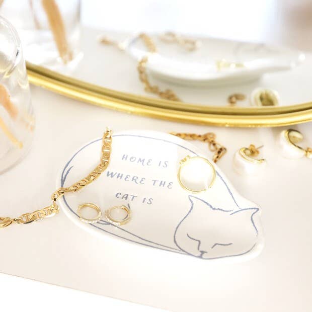 Jewelry set with gold necklaces on a decorative plate featuring a cat illustration and text.