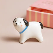 White ceramic dog figurine with a blue collar on a beige background