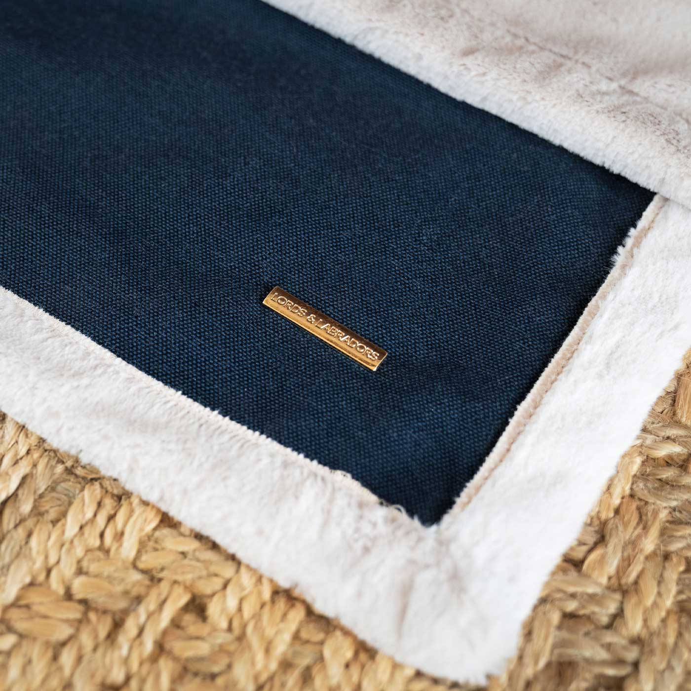 Navy blanket with white trim on a woven surface, featuring a brand label.