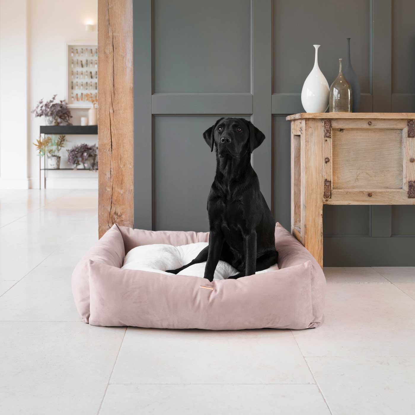 Black dog sitting on a pink dog bed in a modern living room.