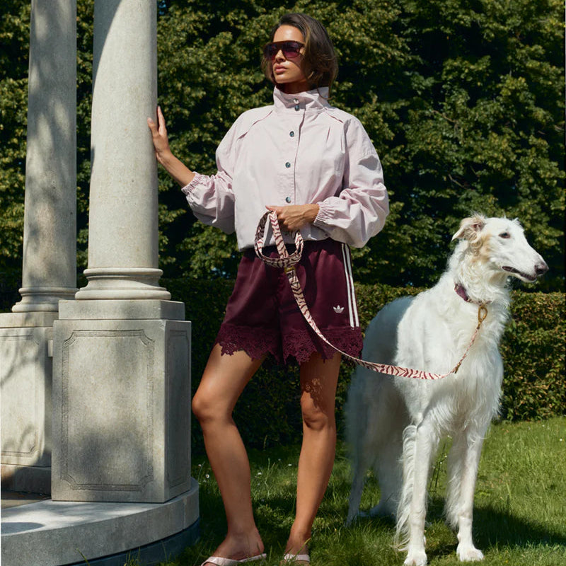 Woman in a garden with a white dog on a leash, standing next to a classical column.