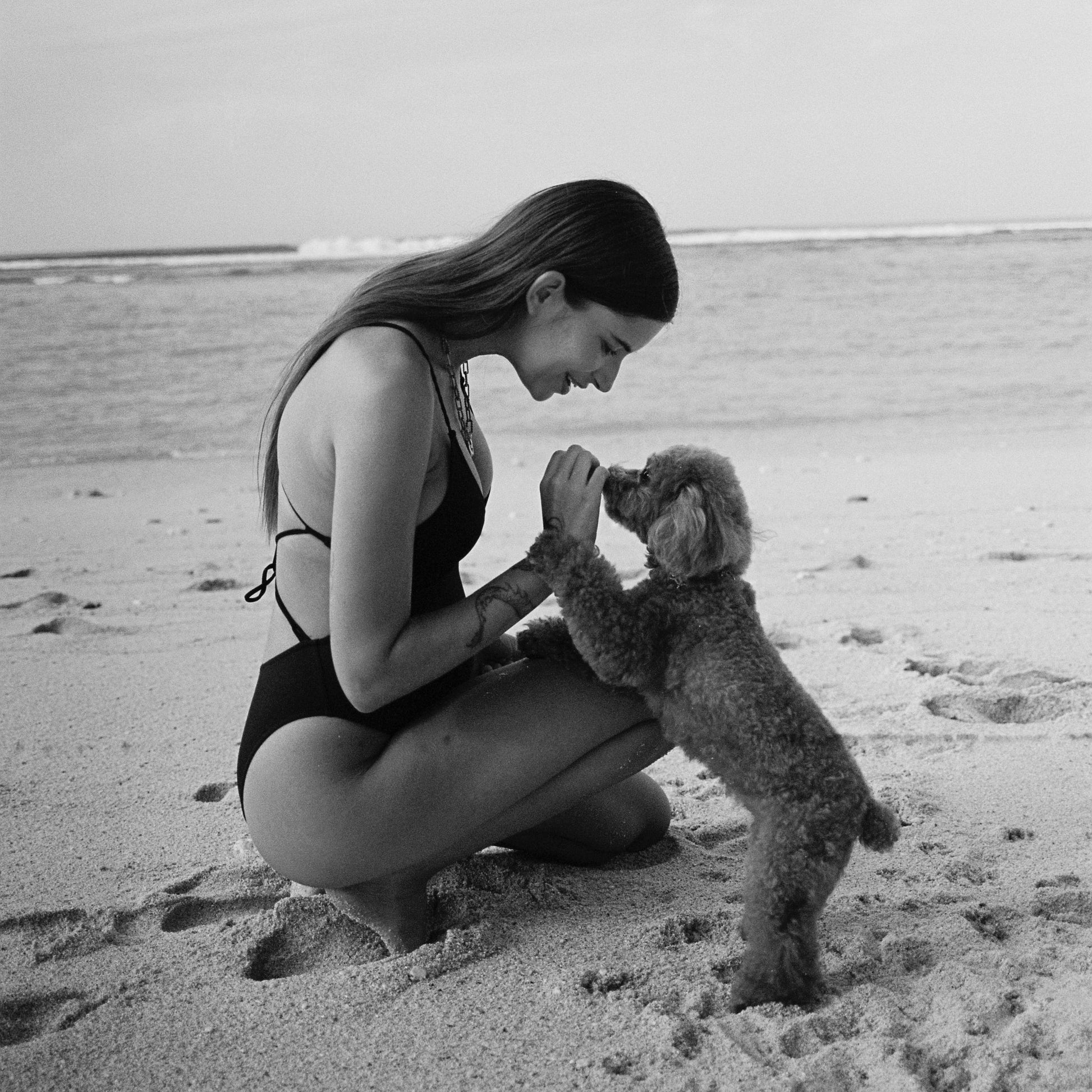 Woman in swimsuit kneeling on beach with small dog