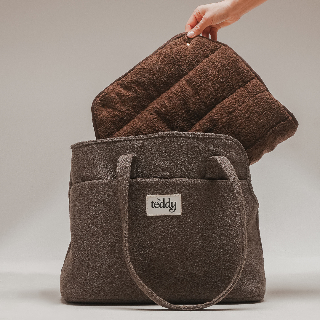 Brown teddy bag with a towel draped over it on a neutral background