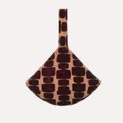A small handbag with a scalloped fan shape and a single top handle, featuring a textured pattern of dark brown and black rectangular spots on a tan background, shown against a plain light gray background.