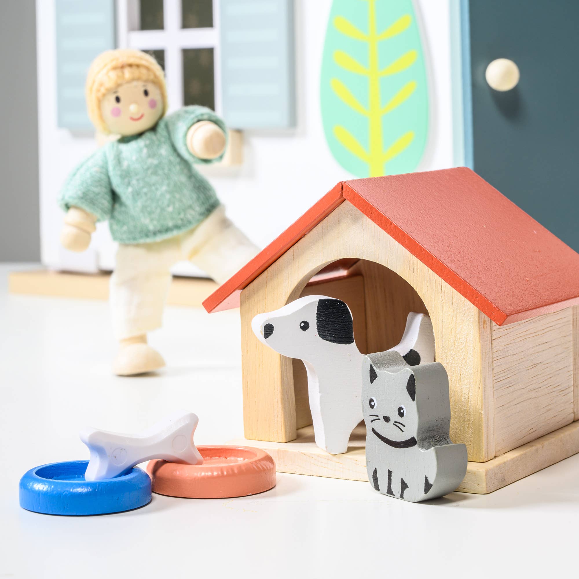 Wooden toys including a doghouse, dog, cat, and fish on a light surface.