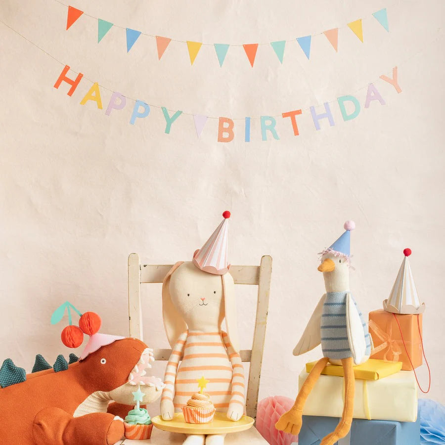 Three stuffed animals wearing party hats sitting on chairs with a 'Happy Birthday' banner above.