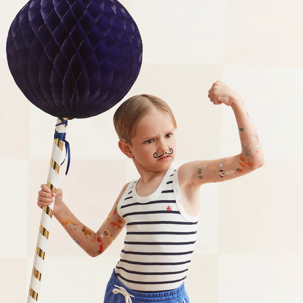 Child flexing arm muscles with a large purple balloon and striped tank top.