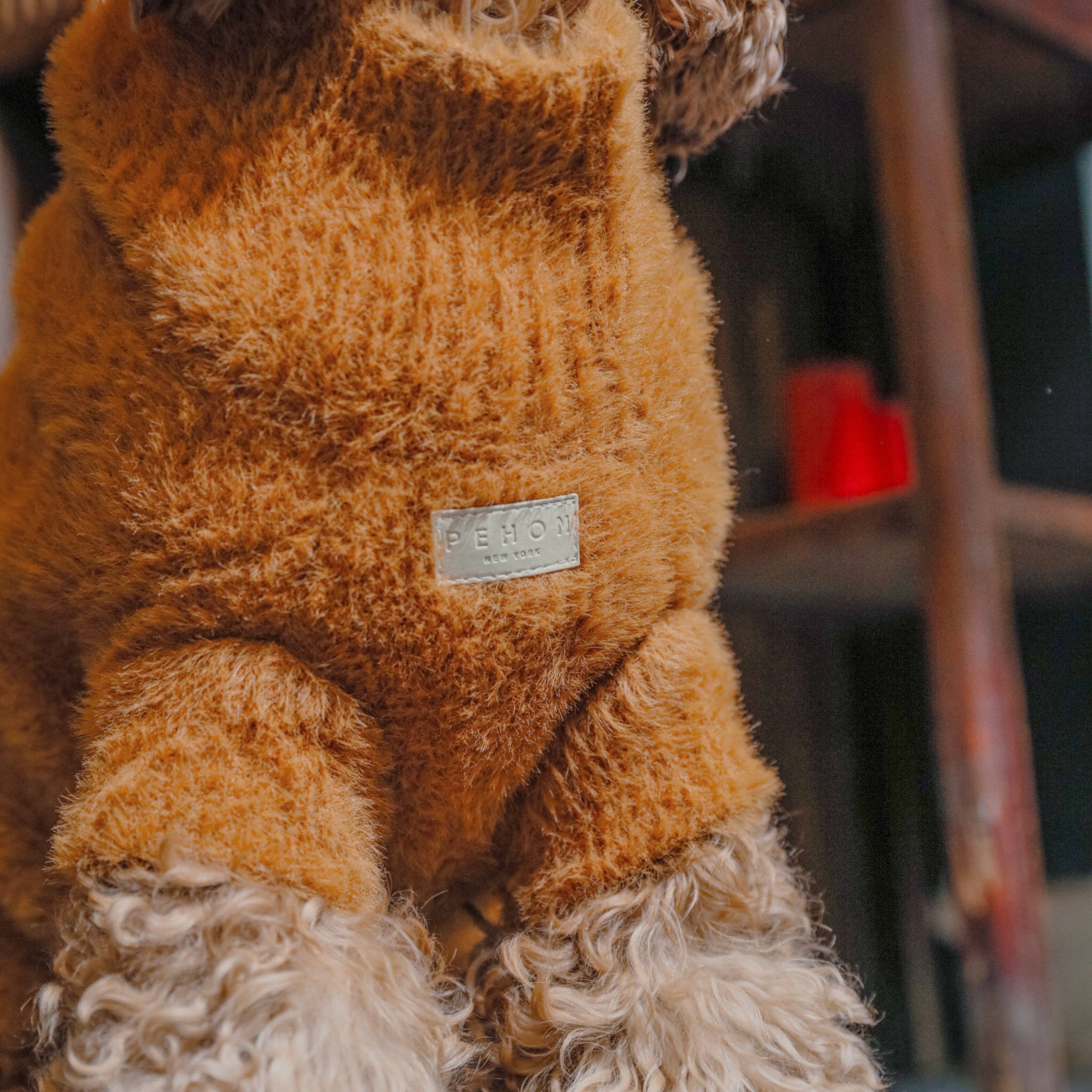 Dog wearing a brown fleece sweater with a brand label, standing indoors.