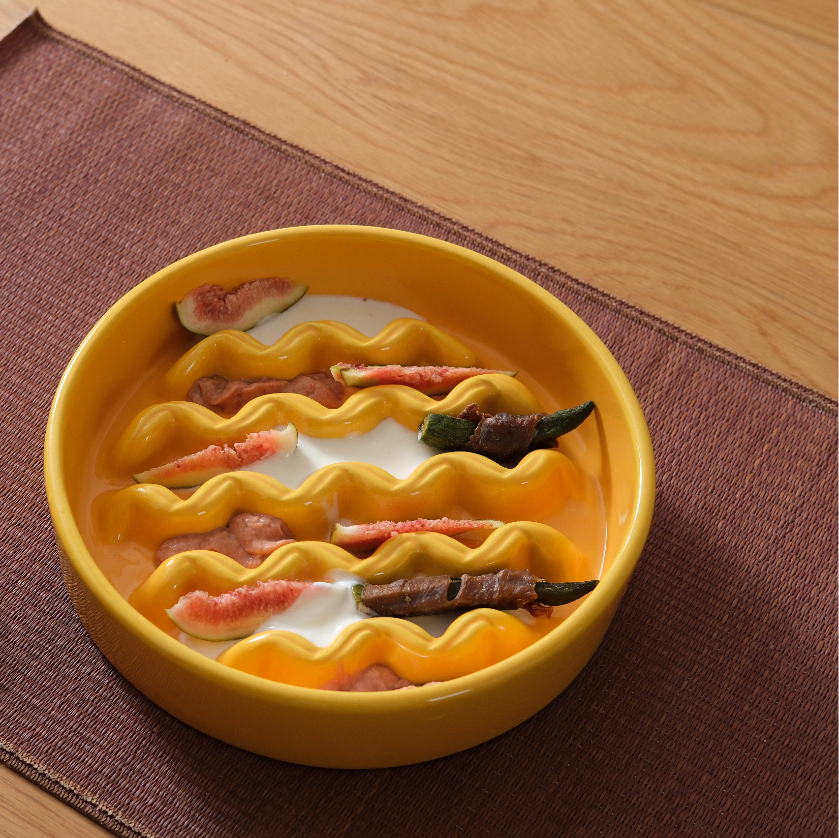 Yellow ceramic dish with wavy design containing food items on a wooden surface.