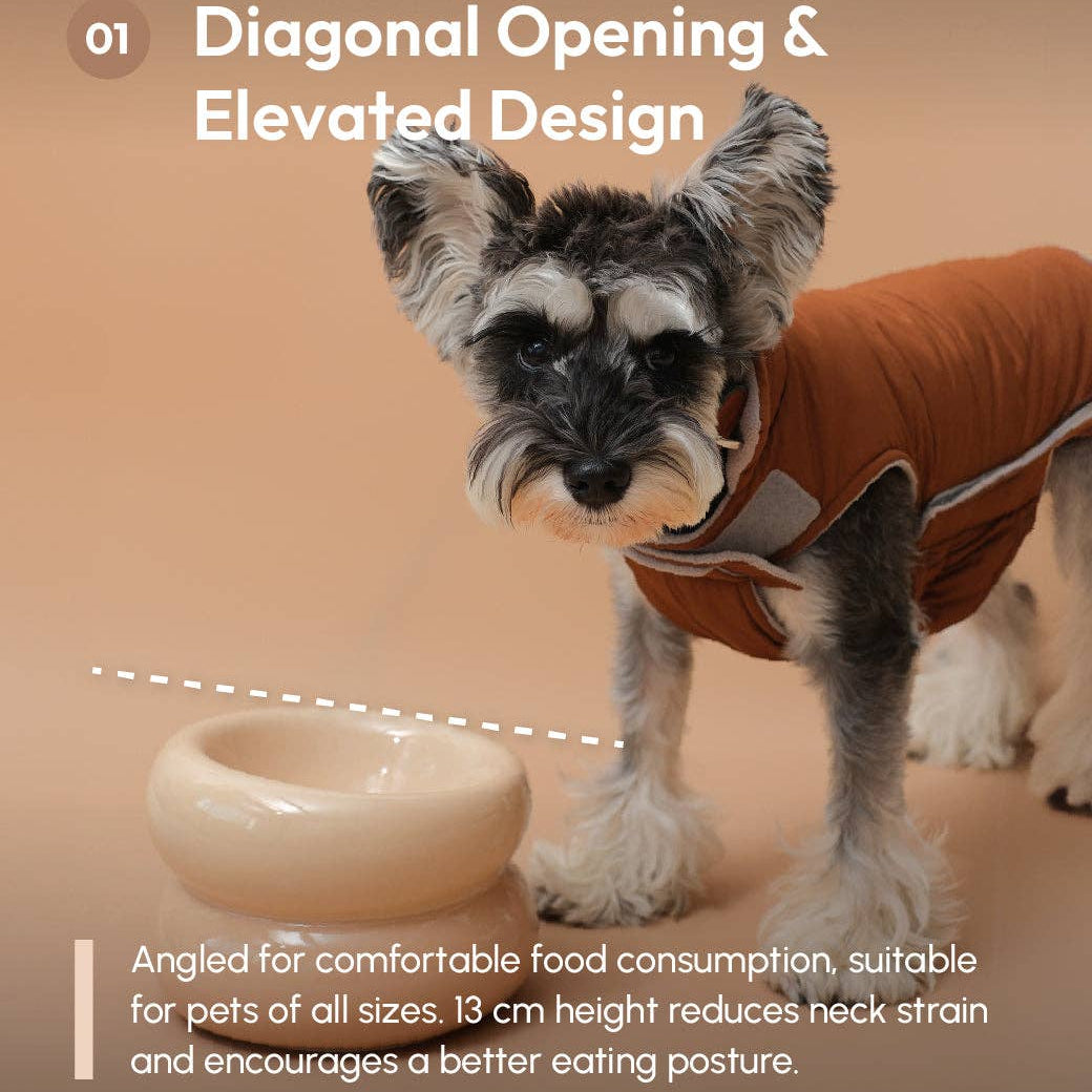Dog wearing a brown coat with a bowl on a beige background, highlighting diagonal opening and elevated design features.