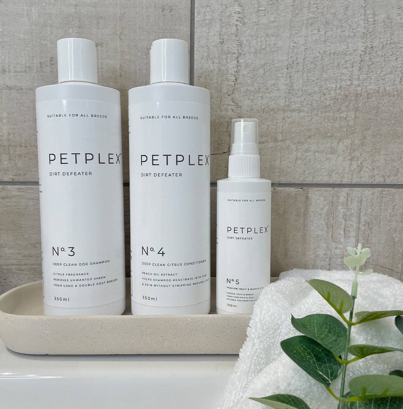 Three Petplex pet care products on a tray with a towel and plant in the background.