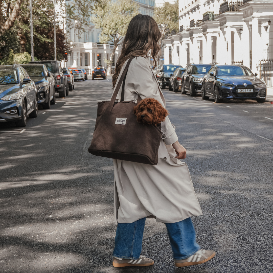 Woman walking down a city street holding a brown tote bag with a visible brand logo.