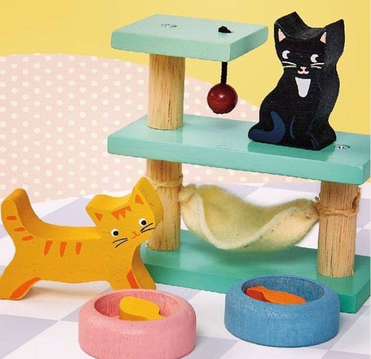 Colorful wooden cat toy with multiple levels, a hanging ball, and cat figures on a polka dot background.